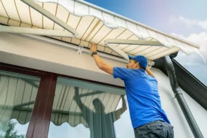 Un uomo ripara un tendone su una casa. Con il bonus tende da sole, le spese possono essere detratte fino al 70%.