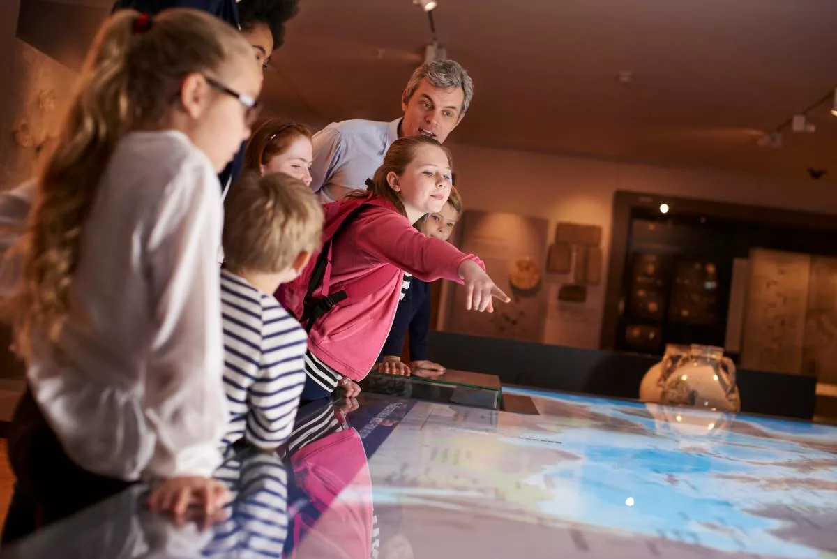 Bambini osservano un display interattivo in un museo. Il bonus gite scolastiche offre sconti fino a 150 euro per i viaggi di istruzione.