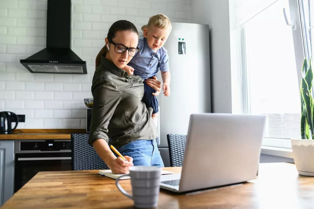 Una donna tiene un bambino mentre è seduta a una scrivania con un laptop: bonus mamme lavoratrici